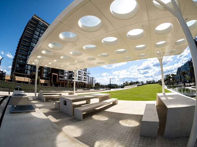 Tables and seating, a barbecue with a sink and food prep area. The solar glass panels are circular insets into square blocks that make up the shade structure.