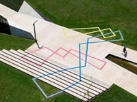 People walking on top of the Stream artwork, embedded in the paving, the artwork is made up of pink, yellow and blue intersecting, asymmetric diamonds that light up at night. 