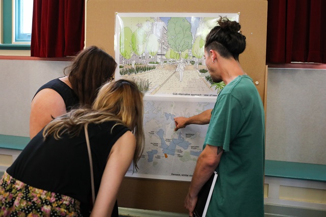 3 adults viewing a map and plans on a board at Alexandria Town Hall.