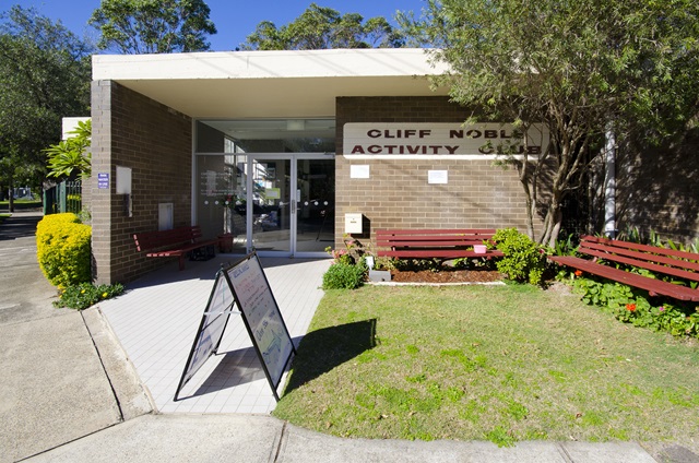 A grassy area and park benches at the front of Cliff Noble Community Centre.
