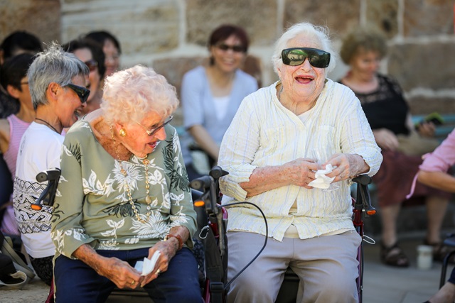 A pair of older ladies sat next to each other laughing.