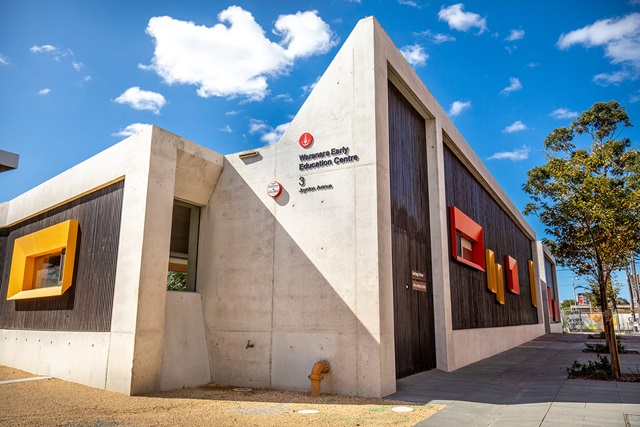 Modern concrete building with colourful window frames and a sign reading "Wananara Early Education Centre" under a clear blue sky.