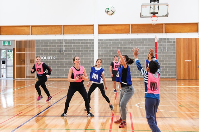 Teens playing netball on an indoor court.