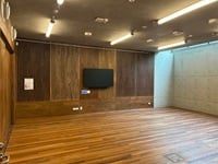 Empty room with wooden floor and walls, a wall-mounted TV, and overhead lighting. Concrete wall on one side.