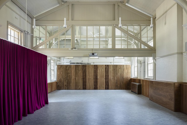 A spacious, bright room with high ceilings, wooden paneling, and a bold purple curtain on the left.