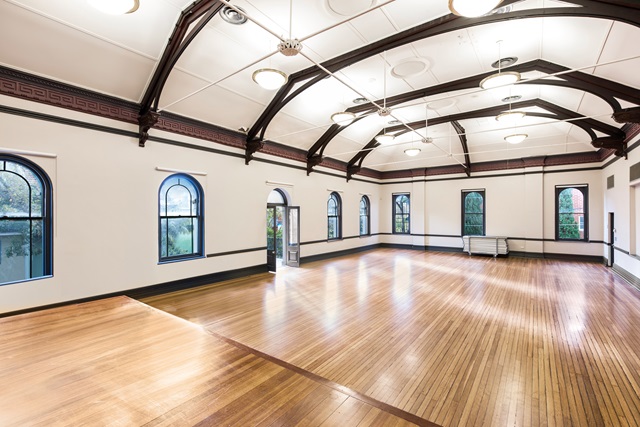 A light-filled, large hall with wooden floor boards, large arched windows and high ceilings.