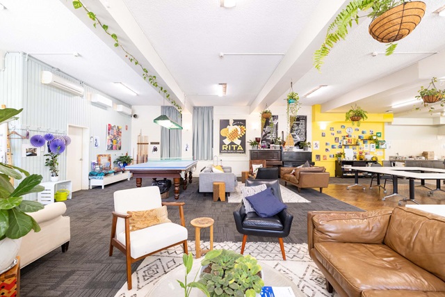 A large room with several couches, chairs, table tennis table and pianos along the back wall