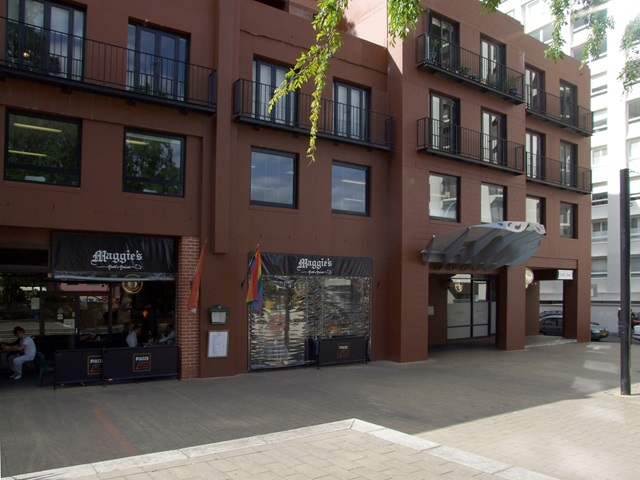 Front of a 3 storey building with a cafe flowing out on to the public sidewalk.