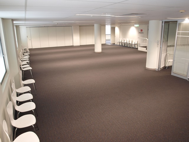 A large room with brown carpet and white chairs on the left.