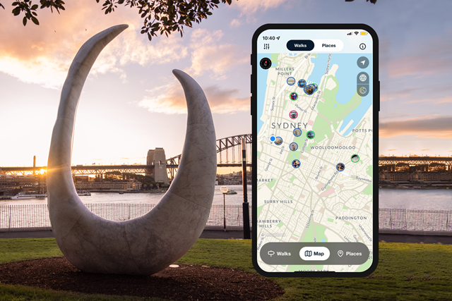 A tall marble curved monument sits on the Tarpeain precinct lawn of the Botanic Gardens. Smartphone mockup shows a map of Sydney on the right. Sun sets behind Sydney harbour and bridge in the background.