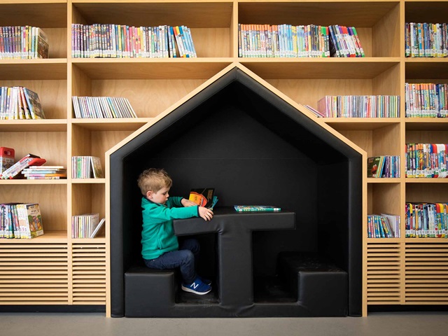 A young boy sits at a table set within a bookshelf.