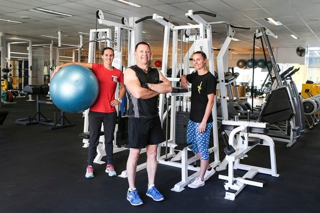 3 people with gym equipment around them, one lady holds a large ball under her arm.