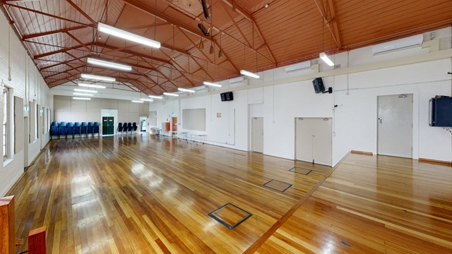 An empty hall with wooden floors., blue chairs stacked against the back wall.