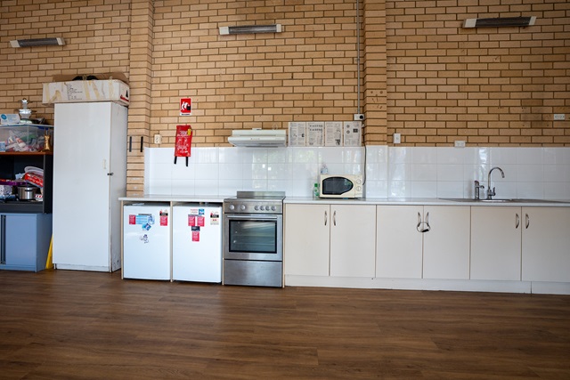 A communal kitchen with a refrigerator, oven, microwave, sink, white cabinets, and brick walls.