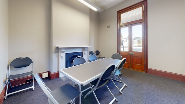 Oblong table with 6 chairs around it in front of a fireplace, 3 chairs against the wall near the fireplace, a wood and glass door, grey carpet