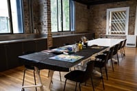 A long table in a room with wooden fllors, 2 windows and a door