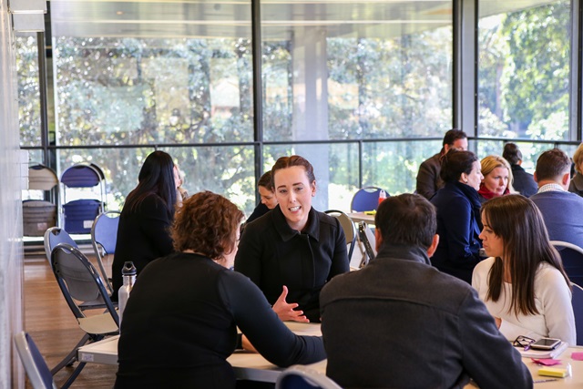 A large room with groups of people sitting at tables talking.