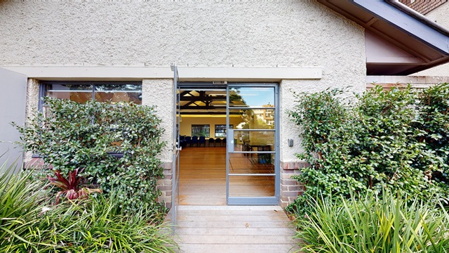 Front entrance with one glass door open, shrubs on either side of the wooden walkway