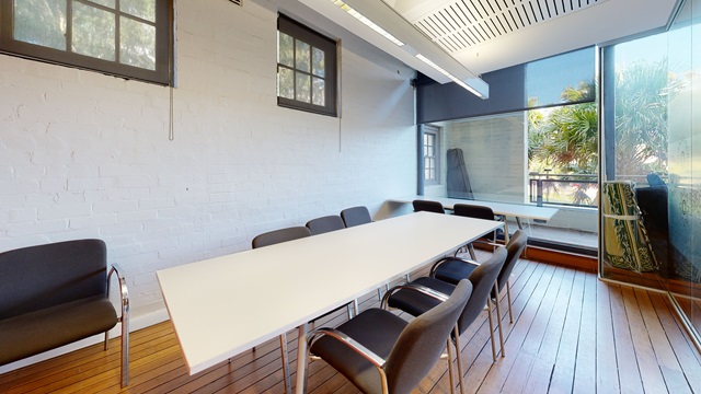 A white table with chairs around 3 sides and 1 chair against the wall, wooden flooring and floor to ceiling windows
