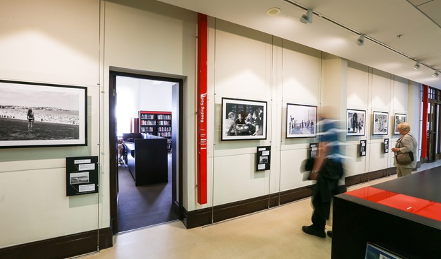 two people, one of them motion blurred, look at a photo exhibition in the library at Customs House. 