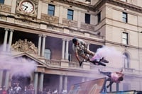 BMX bikers are mid-air off a half-pipe and a large building is in the background. 
