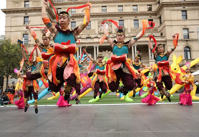 Brightly dressed dancers, mid-air in their dance with Customs House in the background. 