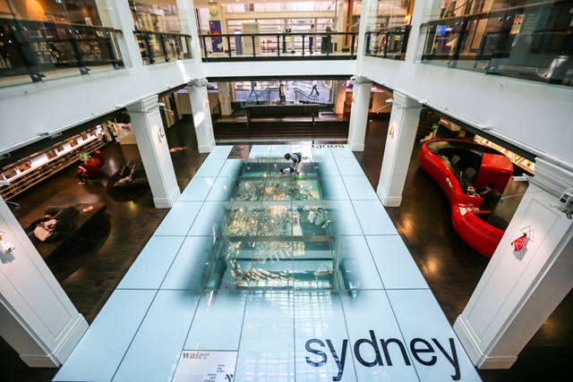 Looking from the mezzanine level down onto a white floor with a model under the glass.