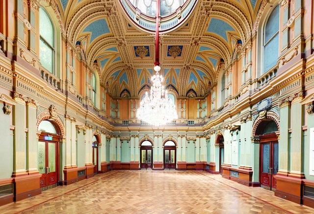 From a high pitched ornate ceiling hangs a chandelier over parquetry floors.