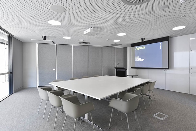 large table square table with chairs around it in front of large wall display