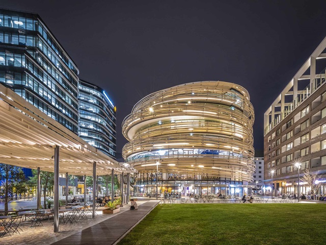 Grass in the front, shade structure on the left, buildings surround and in the background.