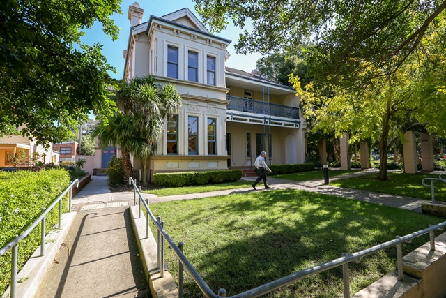 Grass and trees in the foreground and a path with handrails leading to the historic building in the background.