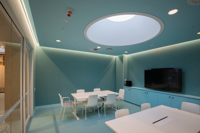 Aqua coloured meeting room with white chairs and tables and a TV screen.
