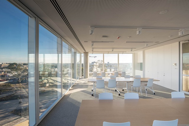 A light, white room with tables and chairs. Two walls are glass, looking over the surrounding area.