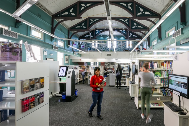 Inside the library as you enter, computer on the right and book shelves either side.