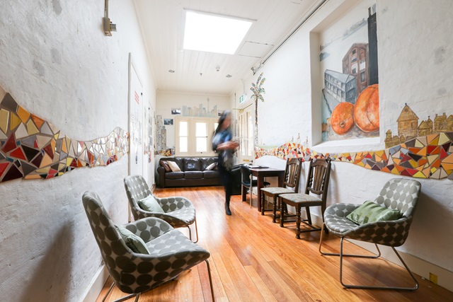 A long room with chairs, painting on the wall and a lady.