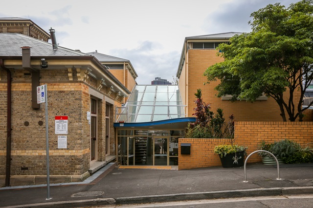 Street view with a footpath and bike rack, and 2 buildings joined together with a glass entry.