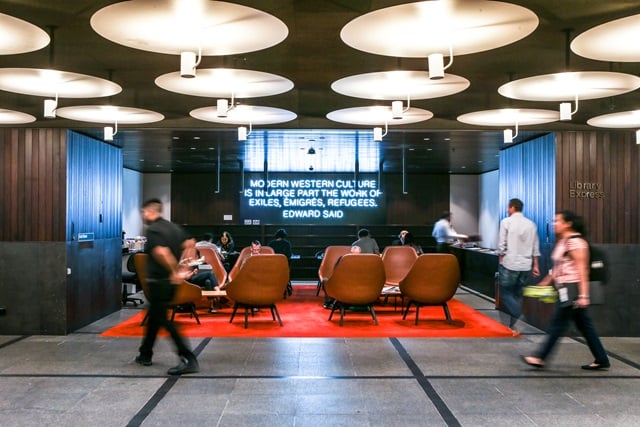 A large area with lights above, people walking past and chairs to sit.