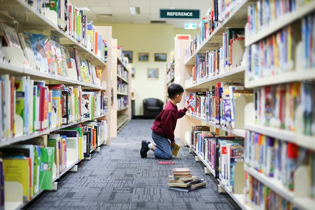 A child looking at books in shelves in a library.