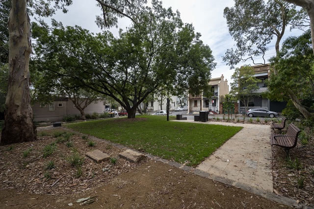 A small park area with a level lawn area surrounded by a stone pathway and trees