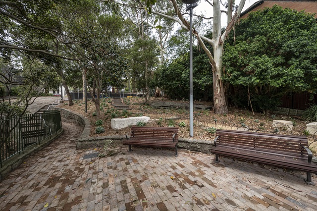 A paved area  within small park with 2 wooden park benches