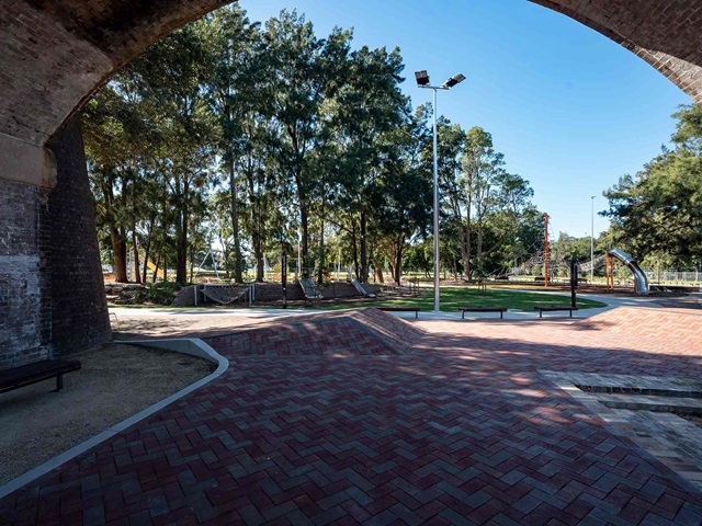 Paved footpath running underneath stone railway arches in a park