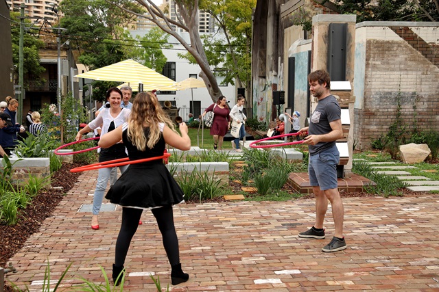 Adults hula-hooping in an outdoor garden.