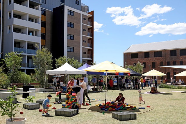 Children and adults sitting under sun umbrellas in Matron Ruby Grant Park.