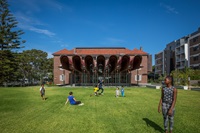 Children and adults playing on grassy area of Matron Ruby Grant Park in front of building.