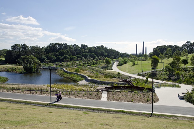View from a high-point looking out over wetlands, walkways, trees and the industrial chimneys in the background.