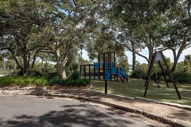 Playground with climbing structures and swings, surrounded by trees and greenery, on a sunny day.