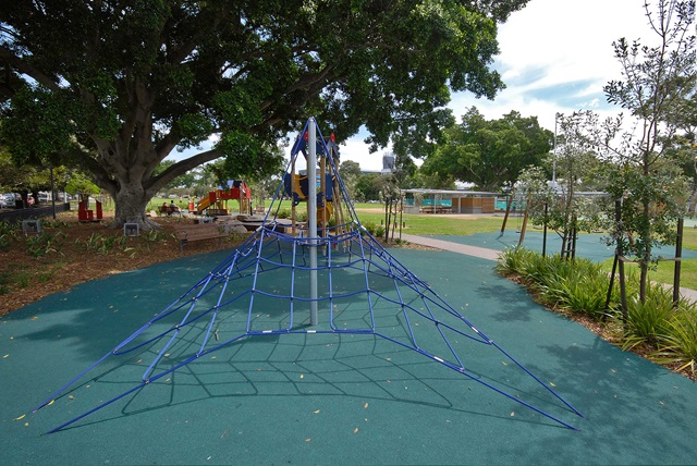 A blue climbing frame shaped like a pyramid on a playground with trees in the background.