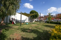 Grass at the front, playground further back and trees to the side, buildings in the background.