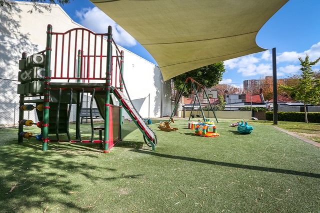 Playground equipment and shade structure above it, building to the left.