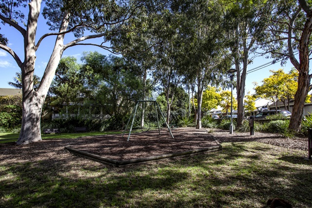 An area of Ernest Pedersen Reserve Playground shaded by tall trees.